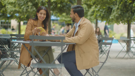Muslim-Couple-On-Date-Sitting-At-Outdoor-Table-On-City-Street-Talking-Together-2